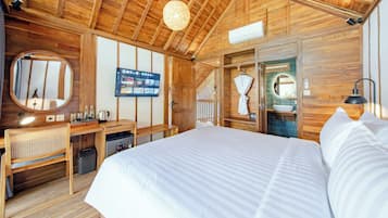 Un dormitorio tipo cabaña de madera con cama, escritorio, televisor y baño visible a través de una puerta abierta.
