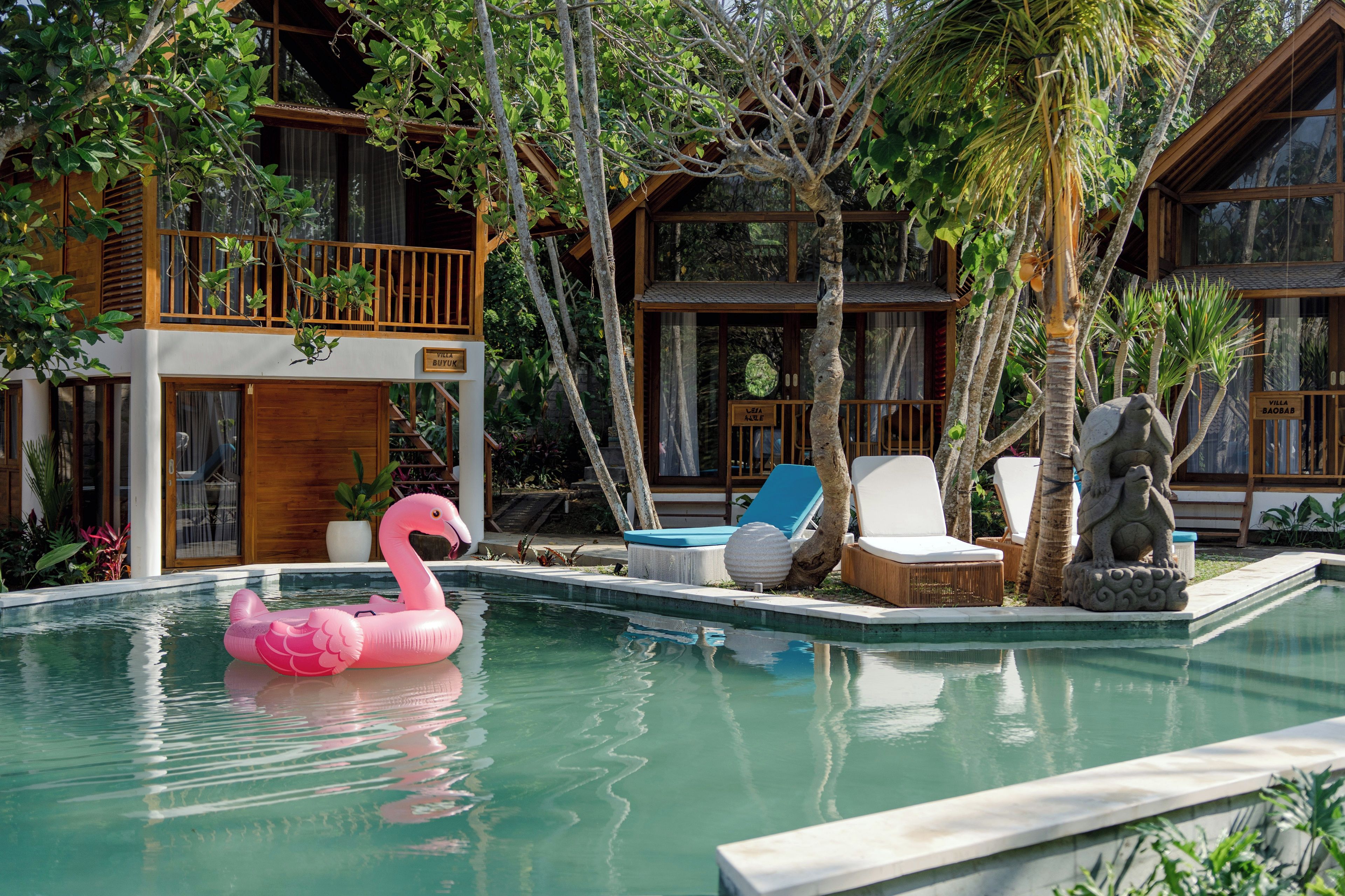 A pool area with a pink flamingo float, lounge chairs, and a stone statue.
