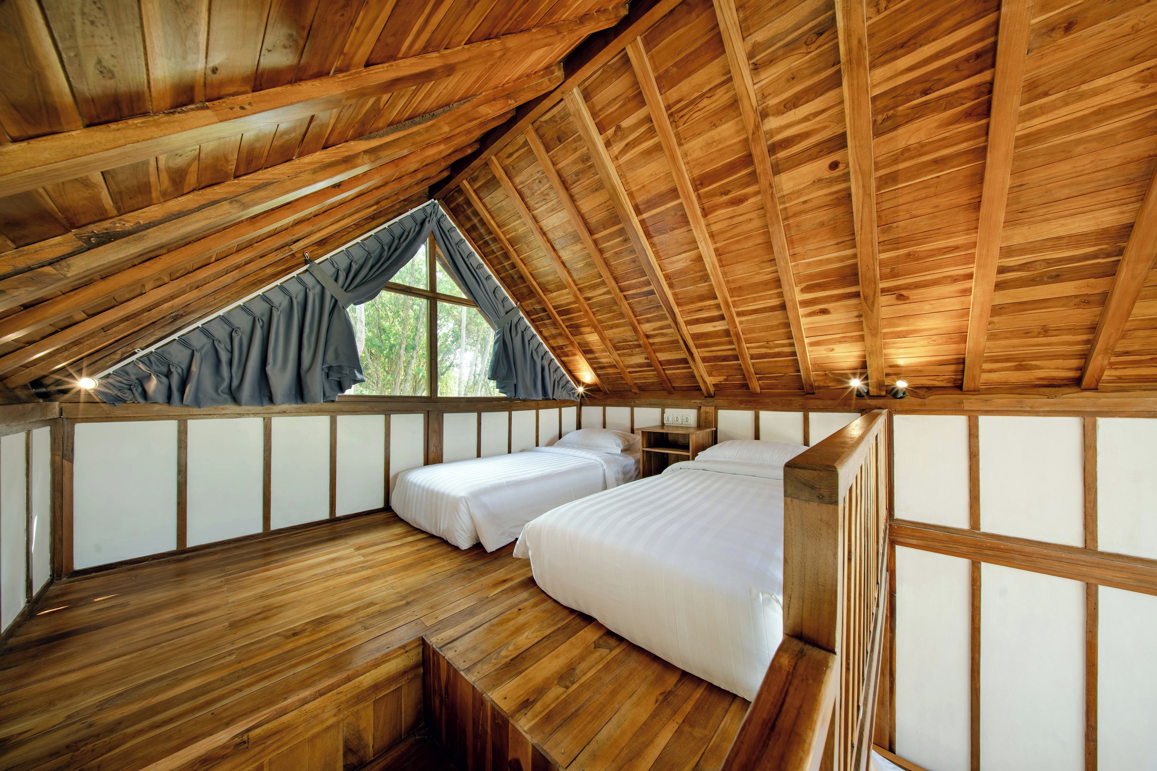 Un dormitorio de ático con piso de madera, dos camas, techo inclinado y una ventana con cortinas.
