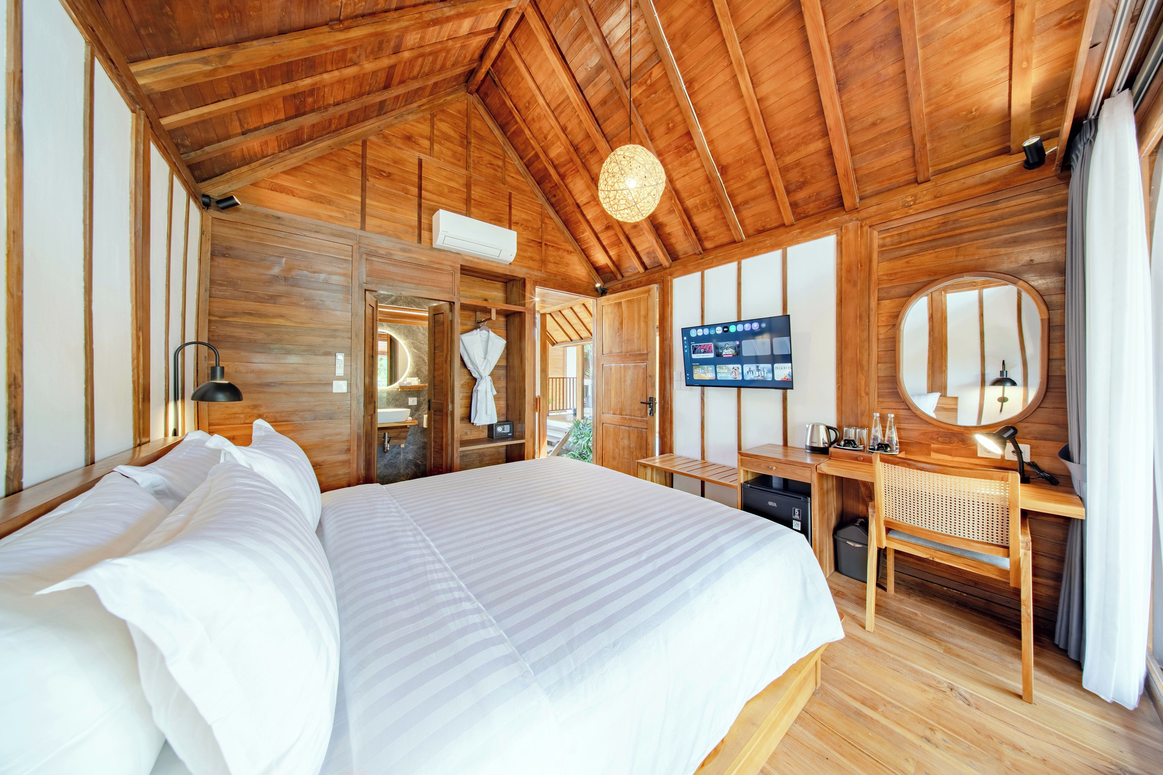 A wooden-floored bedroom with a large bed, a desk, a television, and a mirror.