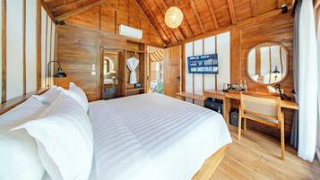 A wooden-floored bedroom with a large bed, a desk, a television, and a mirror.