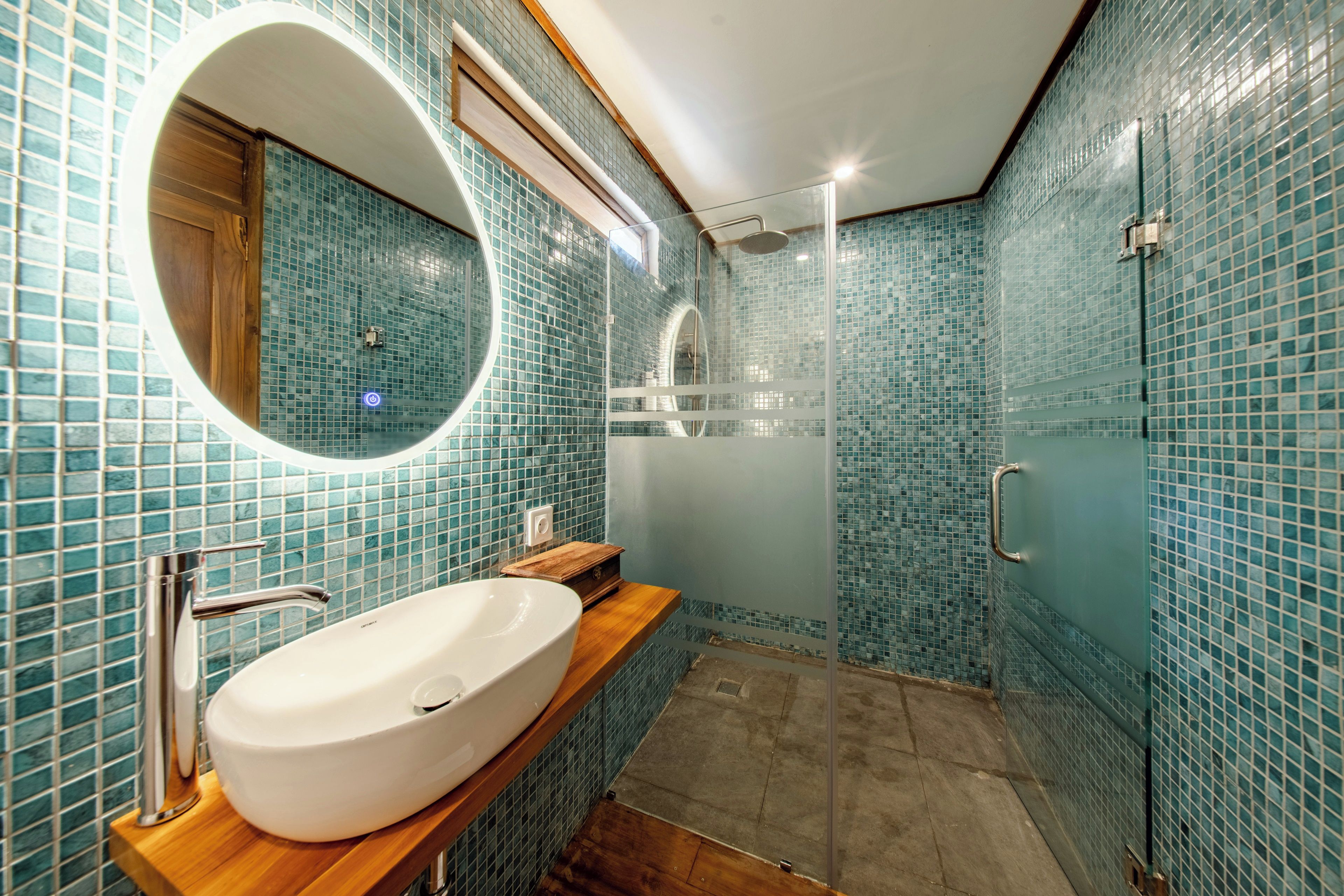A bathroom with a large oval sink, a mirror, and a shower area.