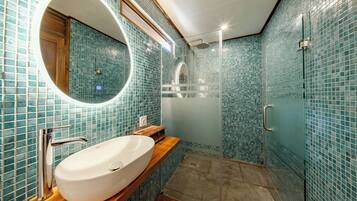 A bathroom with a large oval sink, a mirror, and a shower area.