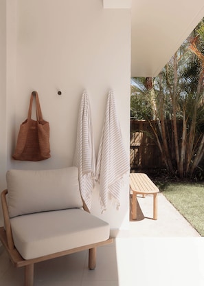 A minimalist outdoor seating area with a sofa and a bench, a woven bag, and two striped towels hanging on the wall. - The Talle II, Palm Beach (Palm Beach)