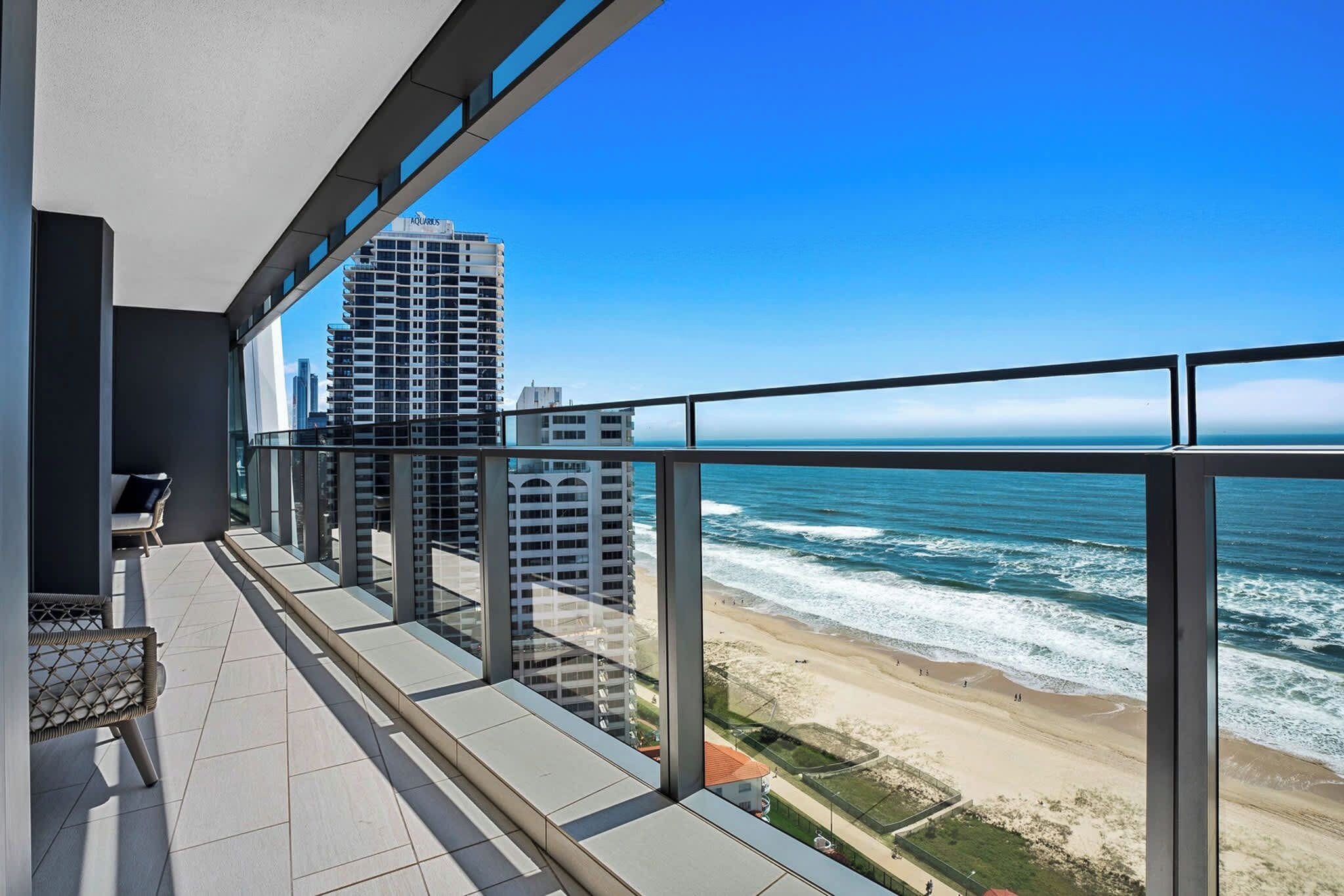 A balcony with a view of the ocean and beach, featuring a chair and a table.