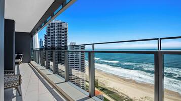 A balcony with a view of the ocean and beach, featuring a chair and a table.