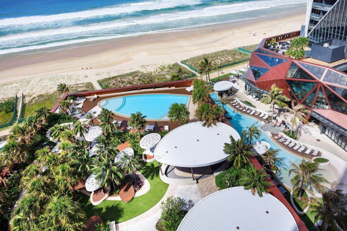 A resort with a large pool, palm trees, and a beach view.
