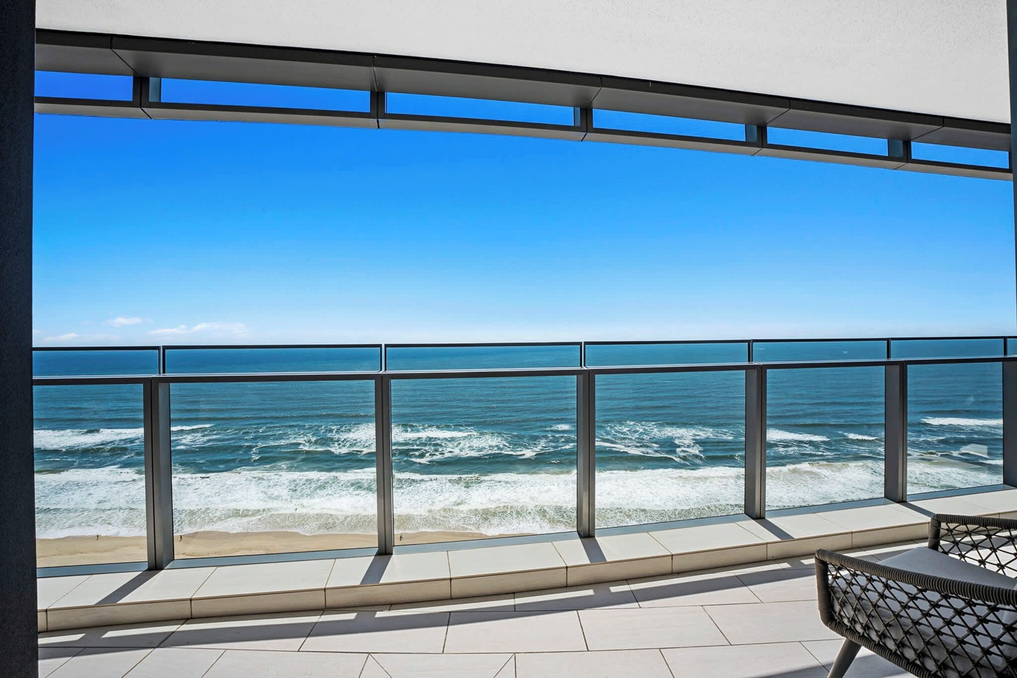 Een balkon met uitzicht op de oceaan, metalen hekwerk en betegelde vloer.