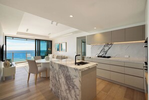 Prepare meals in the contemporary kitchen, with a marble-look island and ocean views beyond the dining area. - Jewel Designer Residence | Direct Ocean Views (Surfers Paradise)
