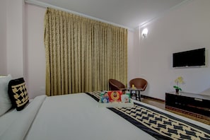 Et hotelværelse med seng, fjernsyn, skrivebord med stol og et vindue med gardiner.