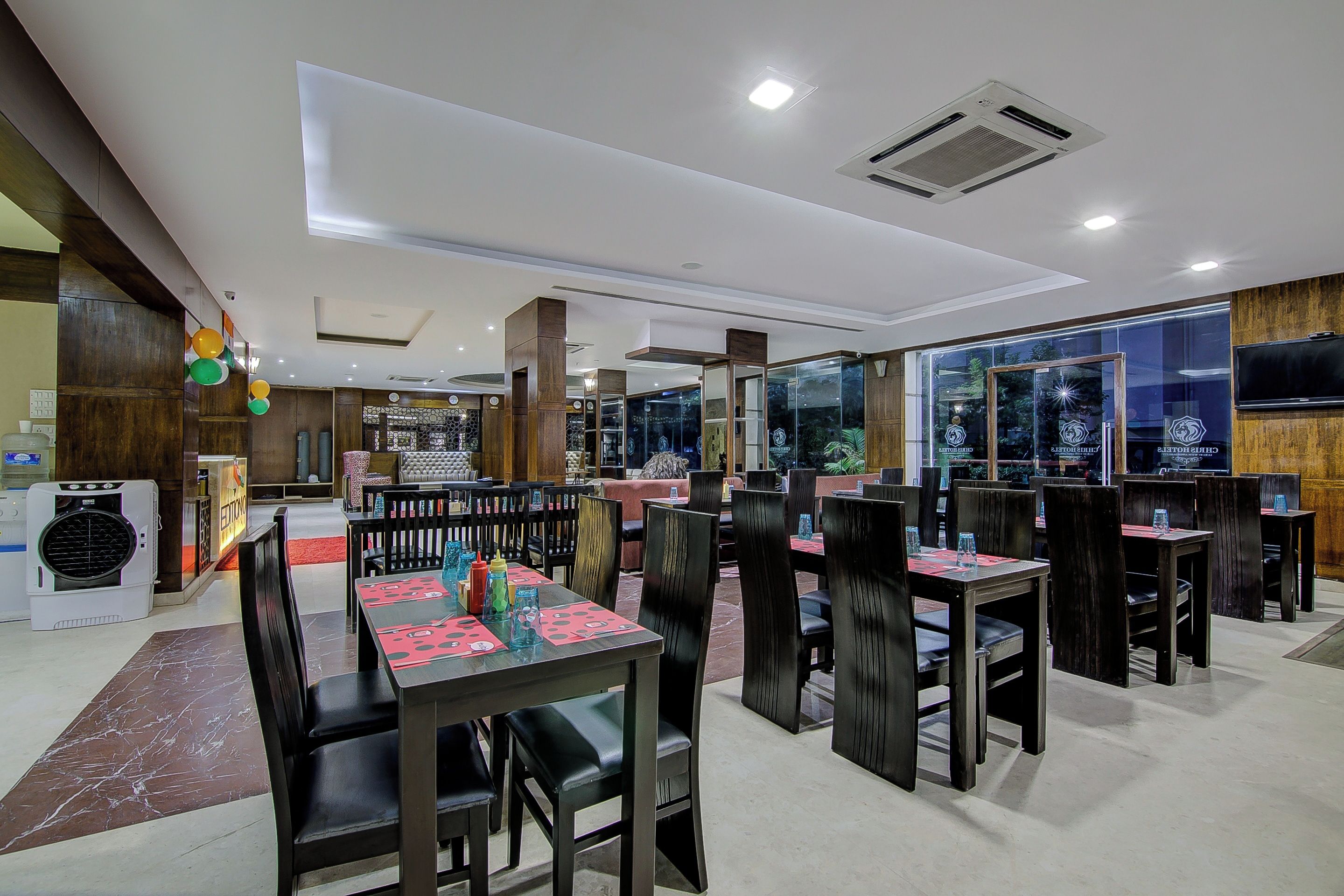 A restaurant with multiple tables and chairs, a large window with a view, and a ceiling with recessed lighting.