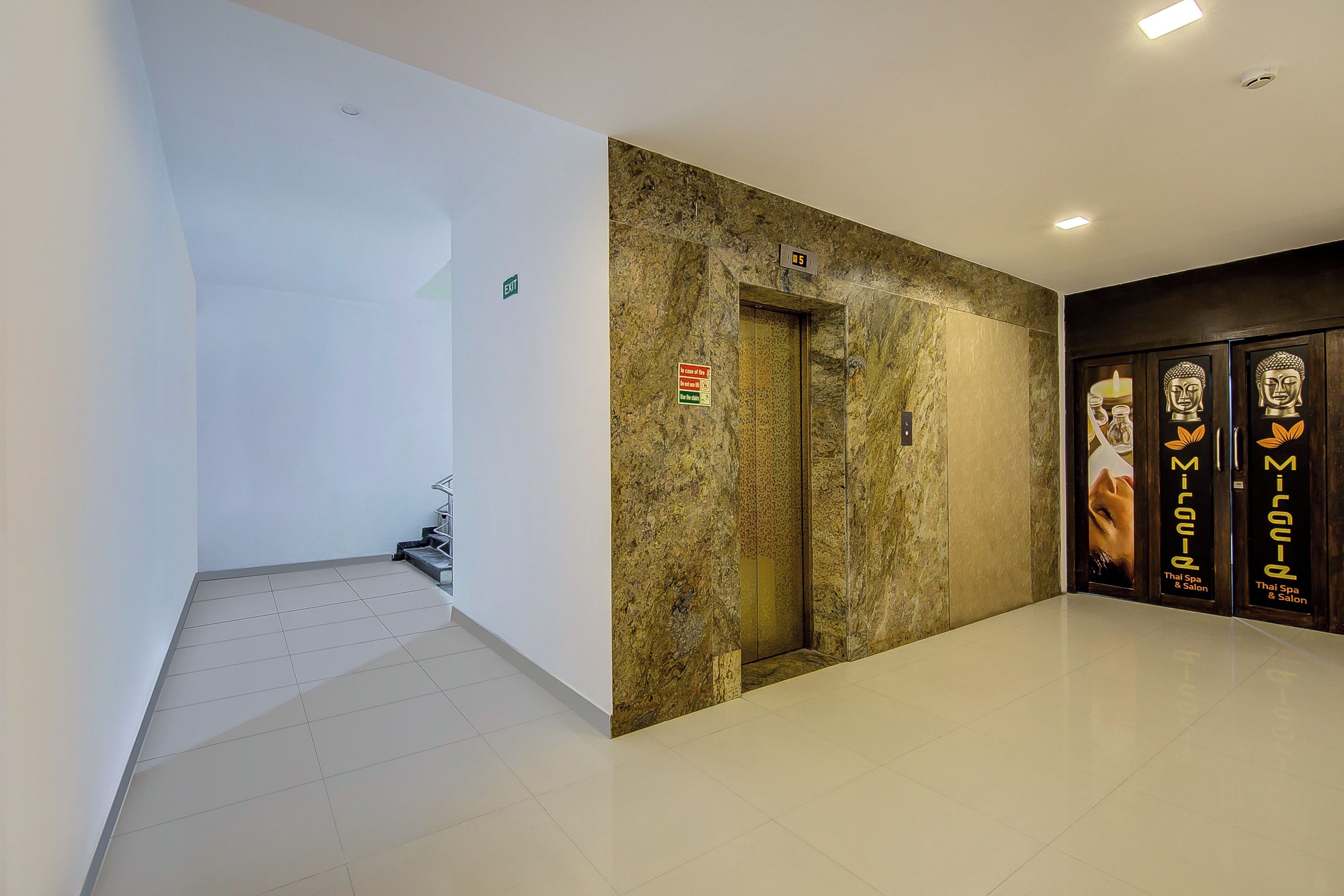 A hallway with a white wall, a marble wall, and a door with a sign.