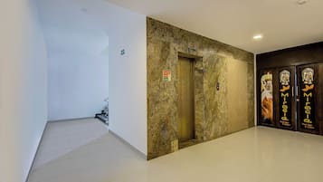 A hallway with a white wall, a marble wall, and a door with a sign.
