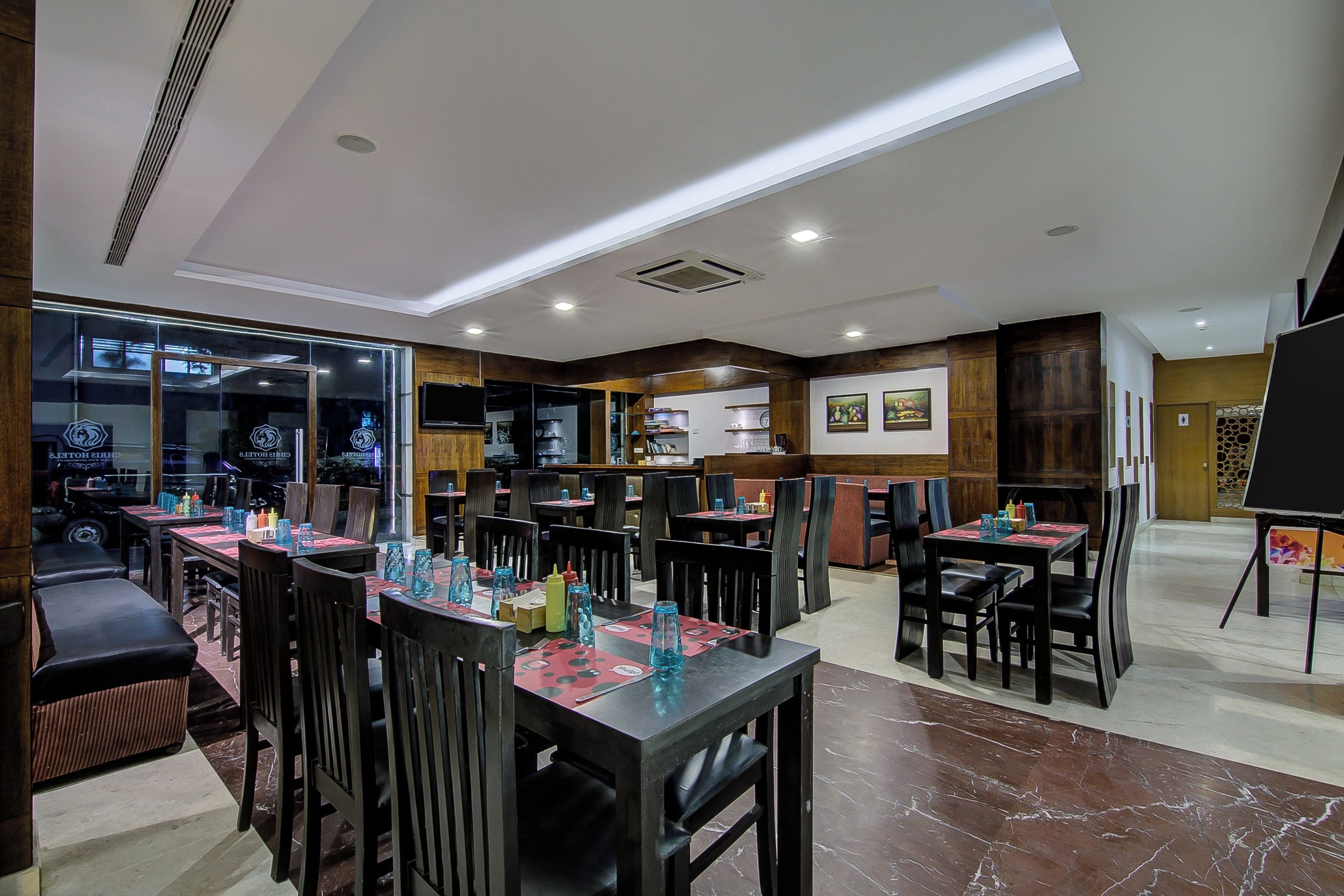 Un restaurante con varias mesas y sillas, una zona de cocina y un ventanal con vistas a la calle.