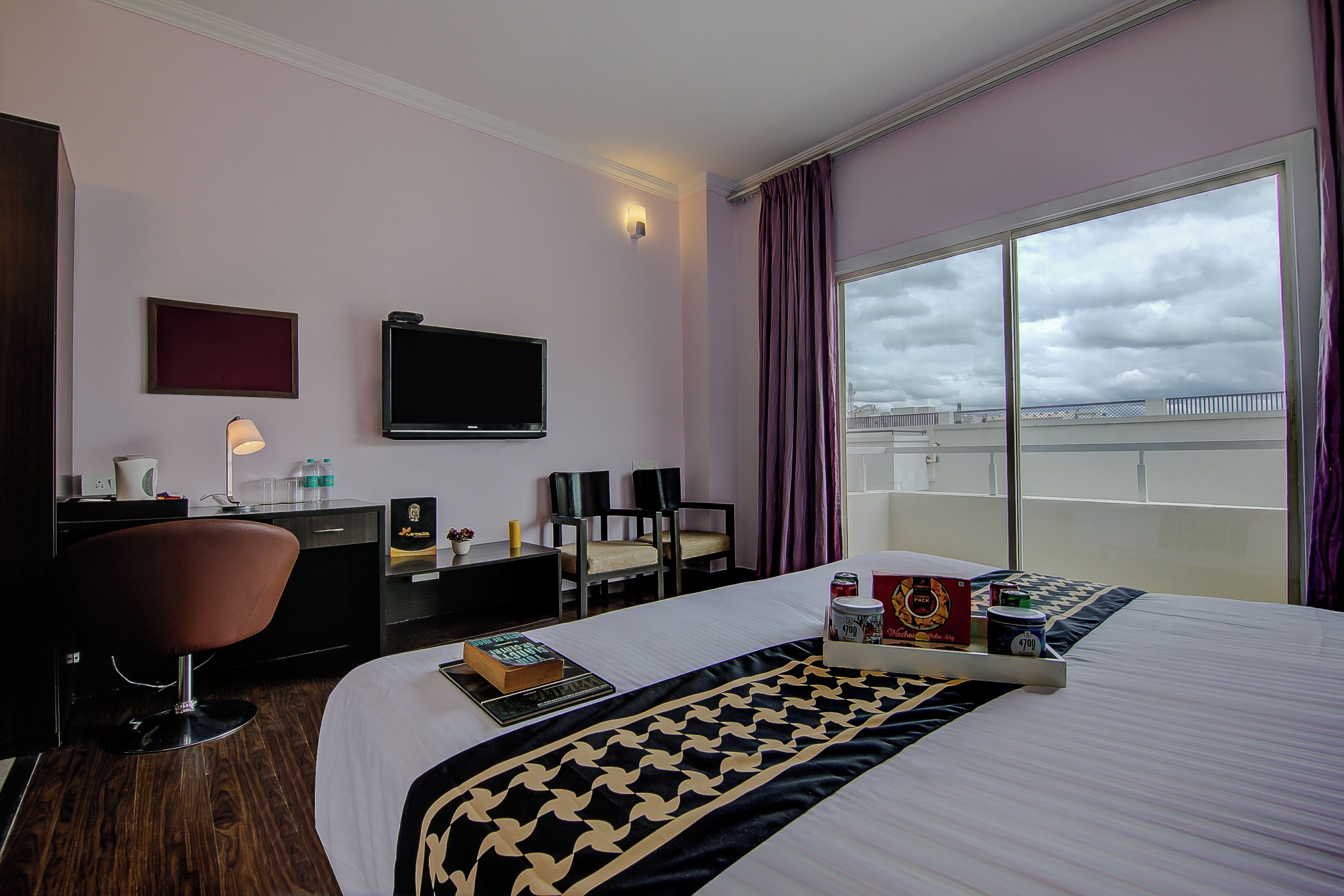 Een hotelkamer met een bed, een bureau, een stoel, een televisie en uitzicht op de stad.
