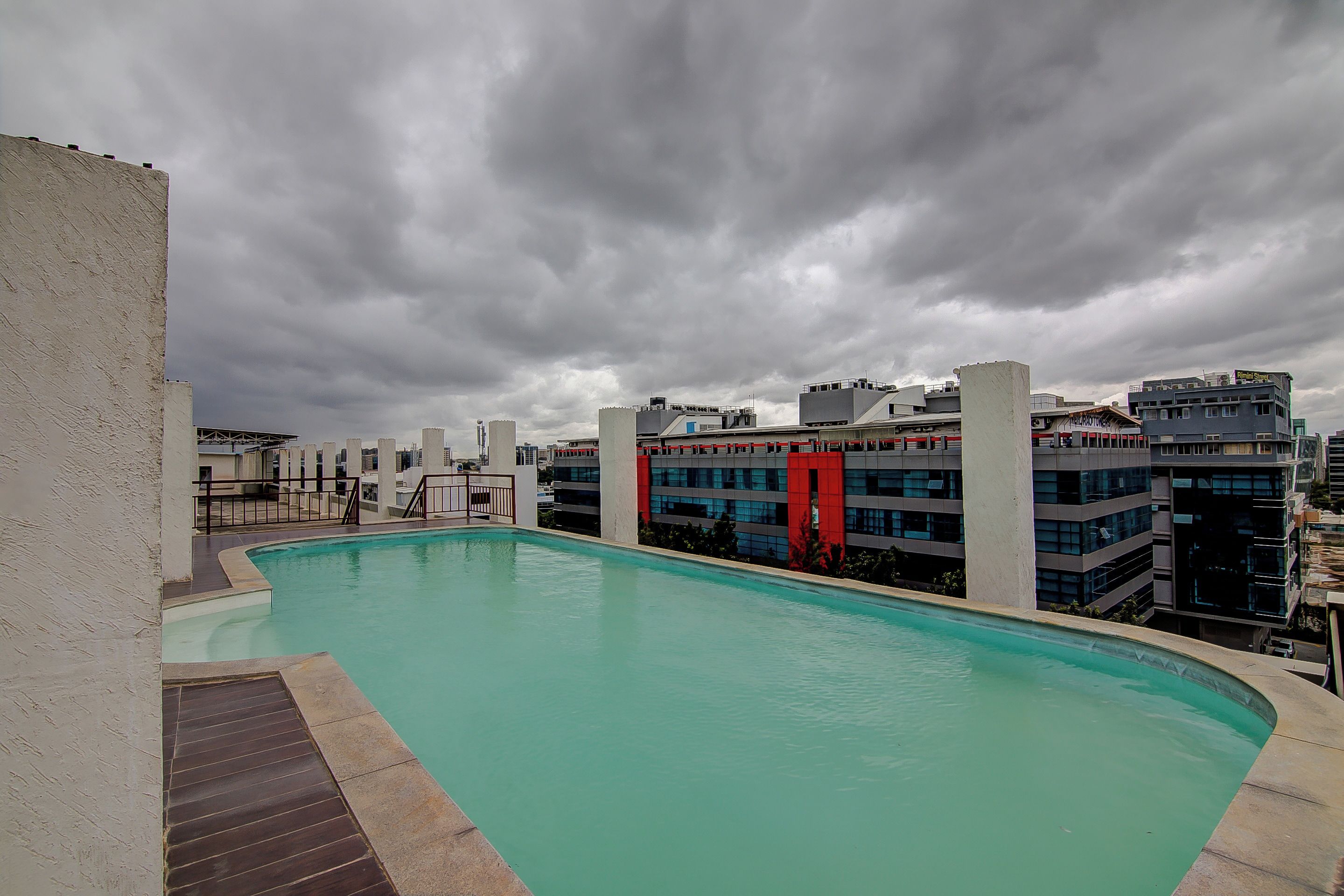 A rooftop swimming pool with a view of modern buildings and a cloudy sky.