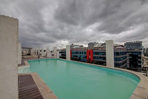 En pool på taket med utsikt över moderna byggnader och en molnig himmel.