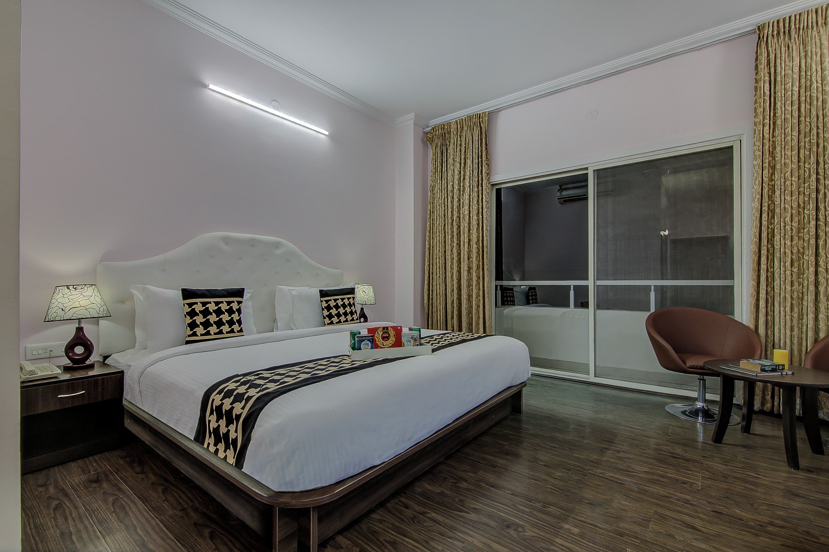 Habitación de hotel con una cama grande, una mesita de noche, un escritorio, una silla y un ventanal corredero al balcón.