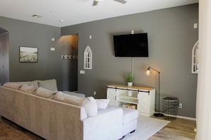 A living room with a sofa, a flat-screen TV, a plant, and a floor lamp. - Inside Anthem master plan community. 8 minute drive to TSMC. Close to I-17! (Phoenix)