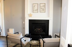 A living room with a fireplace, two framed quotes on the wall, a star decoration, and a small round table with a chessboard. - Inside Anthem master plan community. 8 minute drive to TSMC. Close to I-17! (Phoenix)