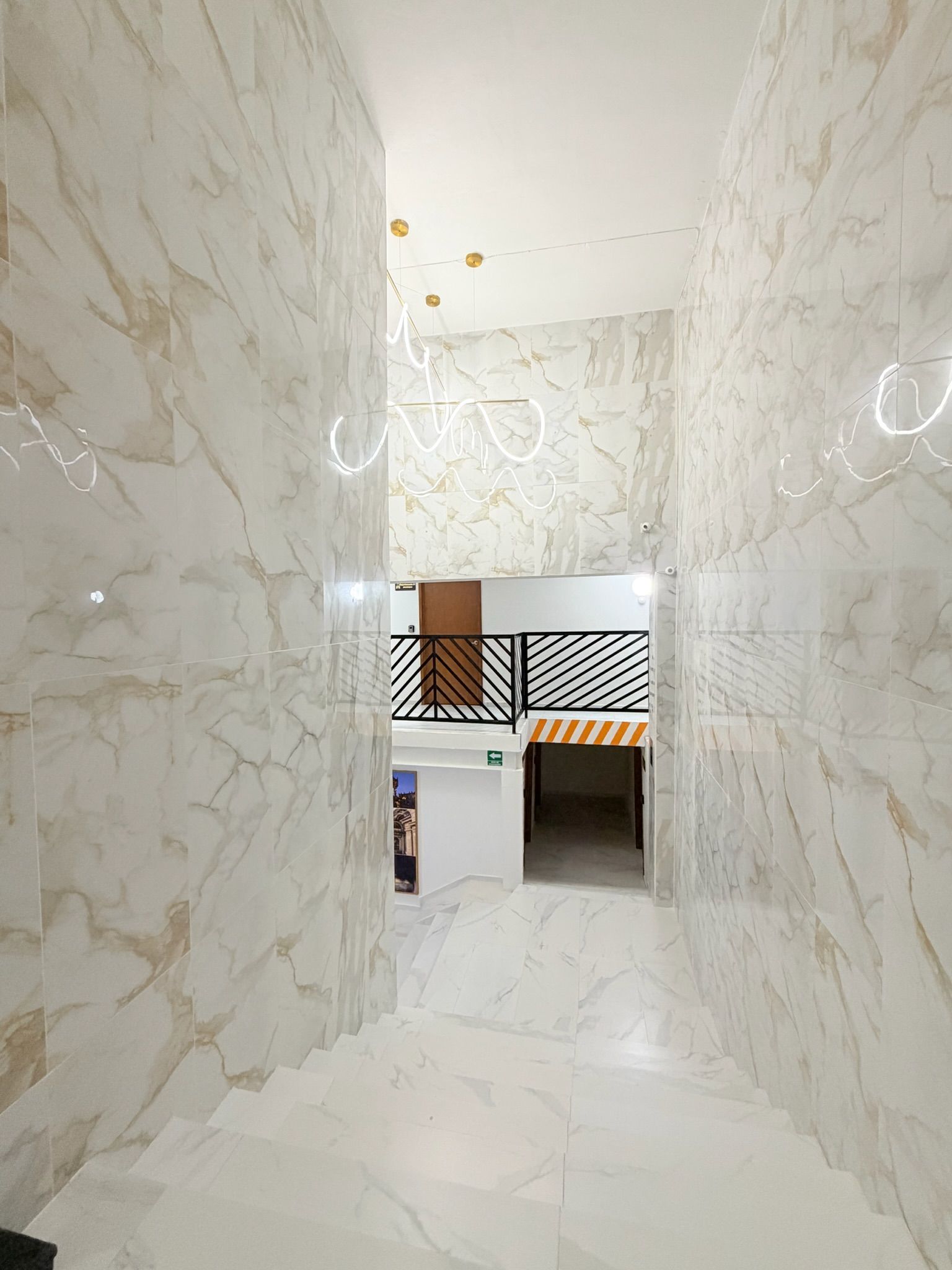 A hallway with marble walls and a staircase leading to a room with a modern design.