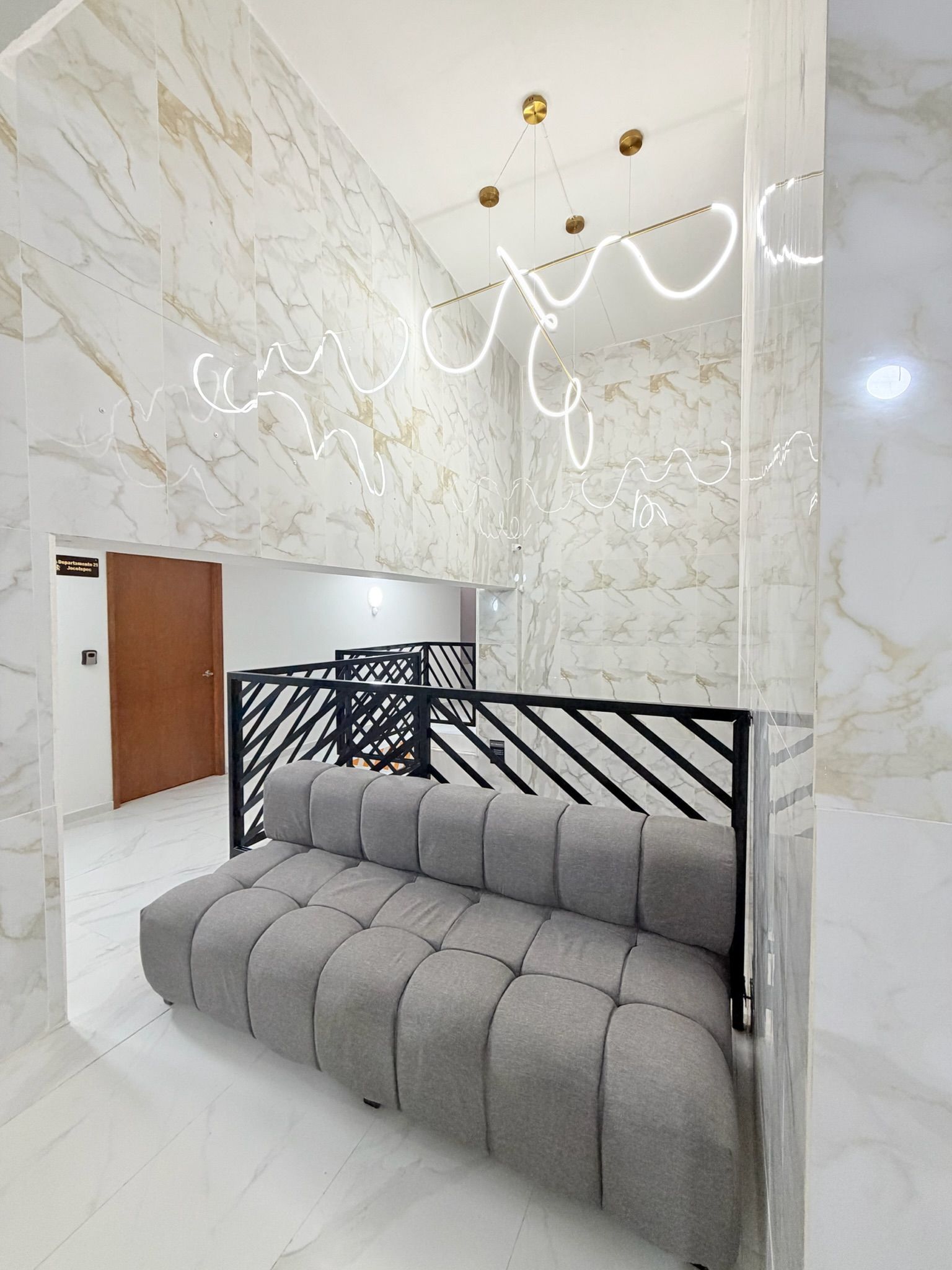 A modern interior with a marble wall, a grey sofa, and a black metal railing.