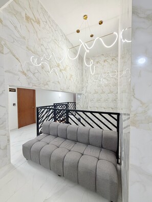 Un interior moderno con pared de mármol, sofá gris y barandilla de metal negro.