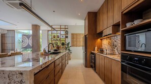 A modern kitchen with wooden cabinets, a marble countertop, and a built-in oven. - Five Palms Villa by Elite Havens  (Mengwi, Badung)