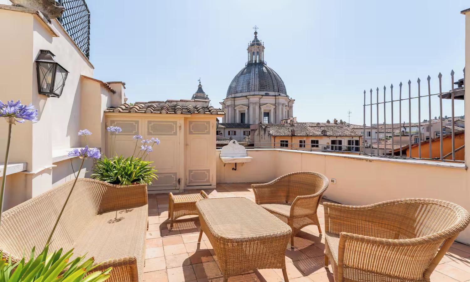 A rooftop terrace with wicker furniture, a potted plant, and a view of a historic building.