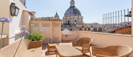 A rooftop terrace with wicker furniture, a potted plant, and a view of a historic building.