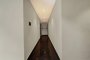 Passadís estret i ben il·luminat, amb parets blanques i terra fosca, que condueix a una porta amb un número.
