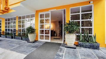 Fachada de hotel amarilla, con amplios ventanales y macetas.