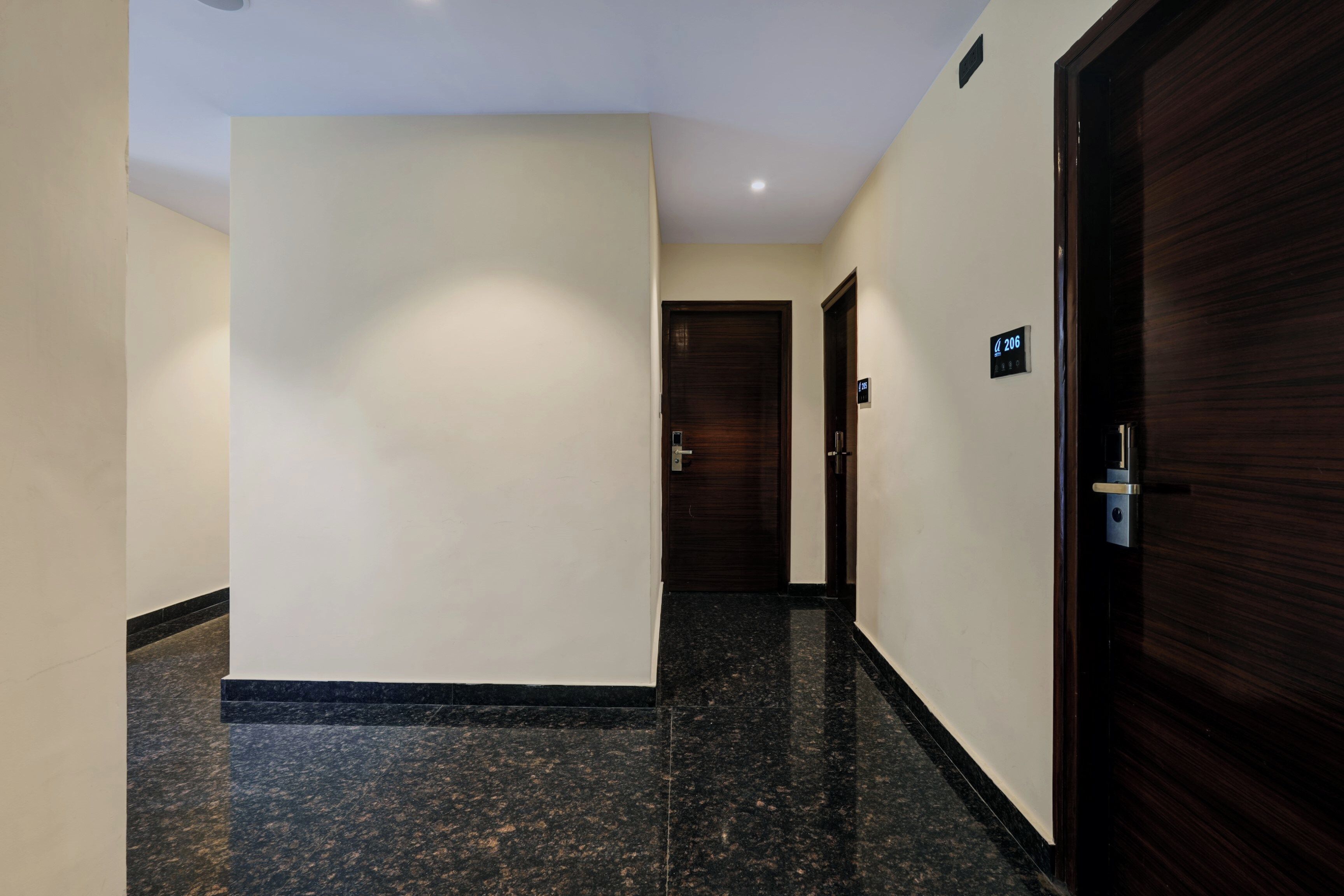 Un pasillo de hotel con piso de mármol, una puerta de madera a la derecha y otra al final.