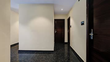 Un pasillo de hotel con piso de mármol, una puerta de madera a la derecha y otra al final.