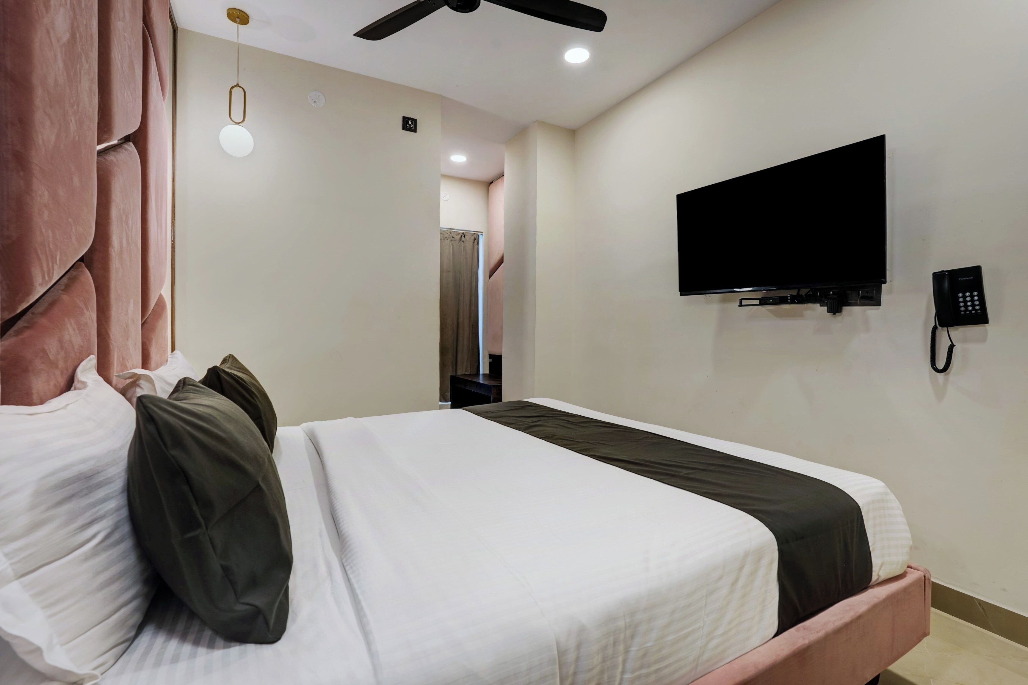 A hotel room with a bed, a television mounted on the wall, a telephone, and a ceiling fan.