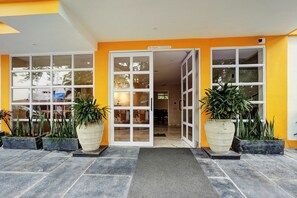 Entrada d'hotel amb façana groga, plantes en testos grans i zona d'entrada enrajolada.