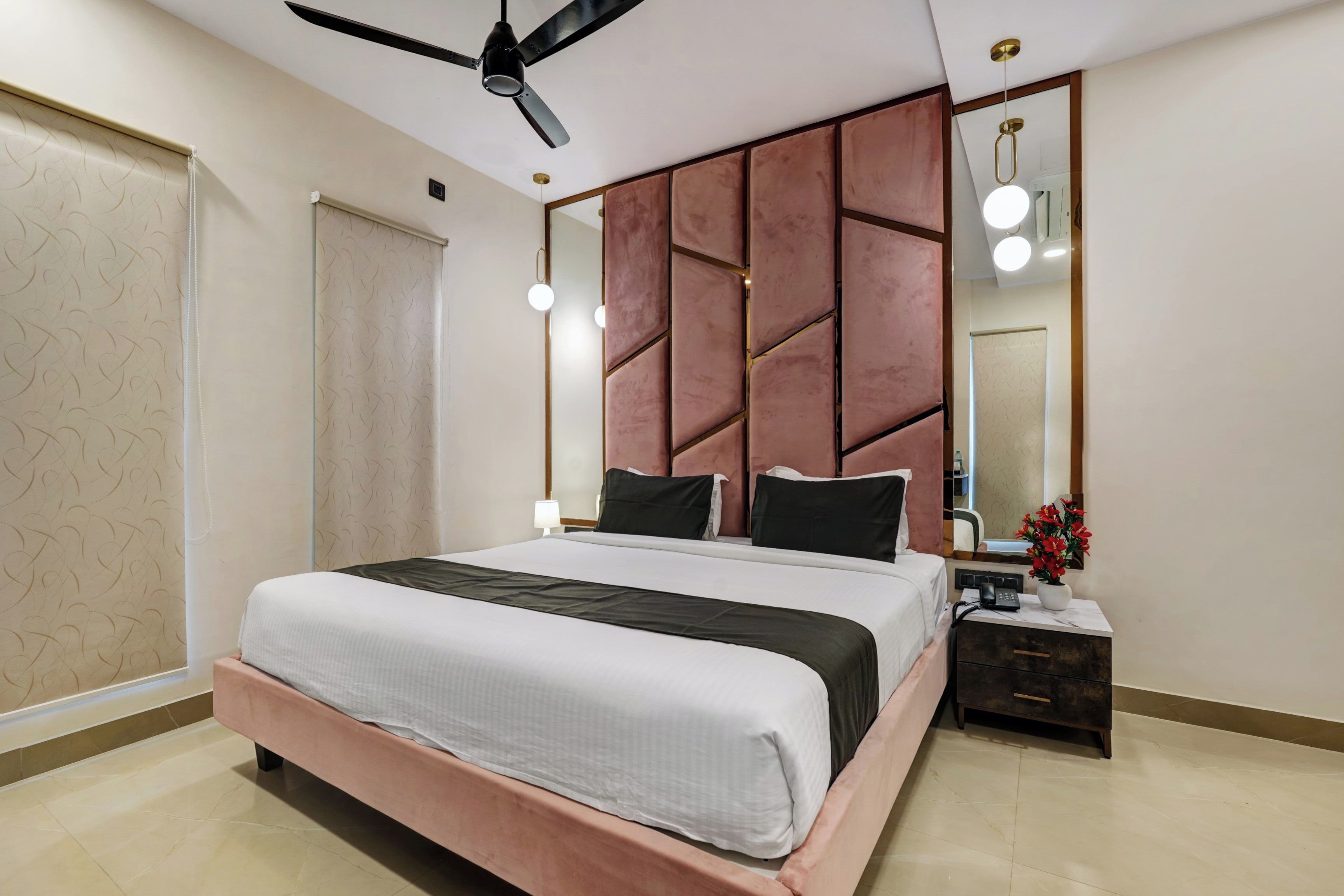 Ein modernes Schlafzimmer mit einem großen Bett, einem Deckenventilator, einem Nachttisch mit Lampe und einem Spiegel.