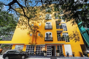 Un edificio de varios pisos con balcones, grandes ventanas y un coche estacionado adelante.