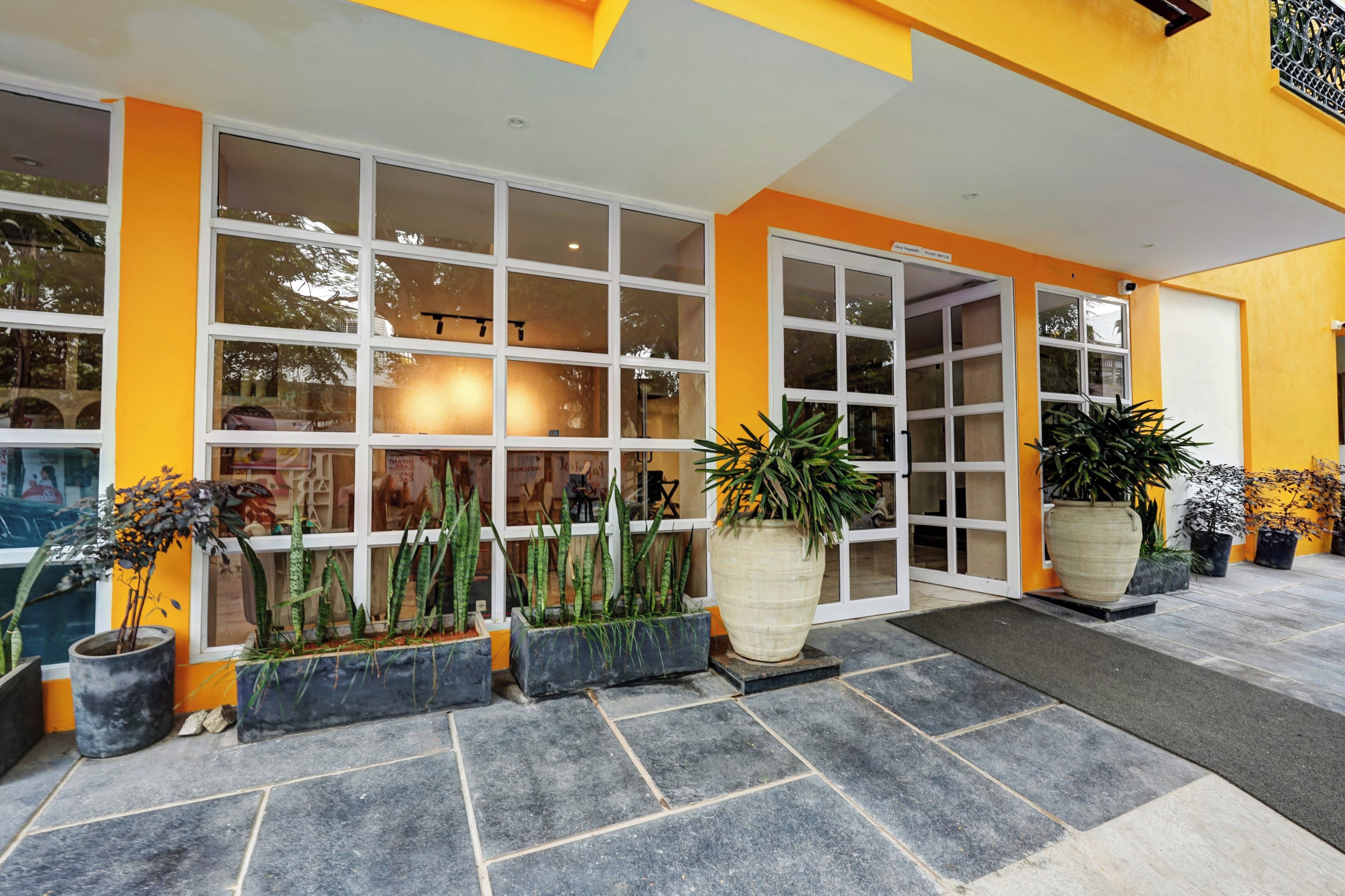 Fachada de hotel amarilla, con grandes ventanales y plantas en macetas.