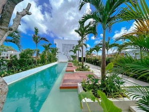 A swimming pool with wooden deck walkways, surrounded by tropical plants and palm trees. - AKA Seseh Living (Badung)