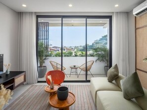 Una sala moderna con sofá, una mesa de centro y un mueble para la televisión. Hay un balcón con vistas a los alrededores.