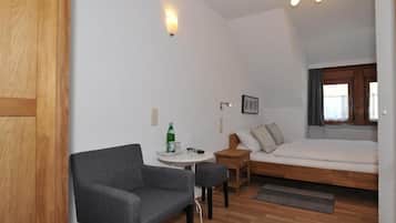 Habitación pequeña con cama, una mesita, una silla y ventana con cortinas.