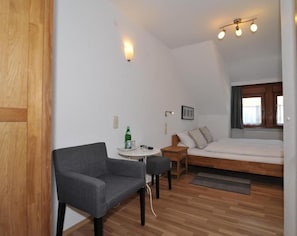 A compact room with a bed, a small table, a chair, and a window with curtains.