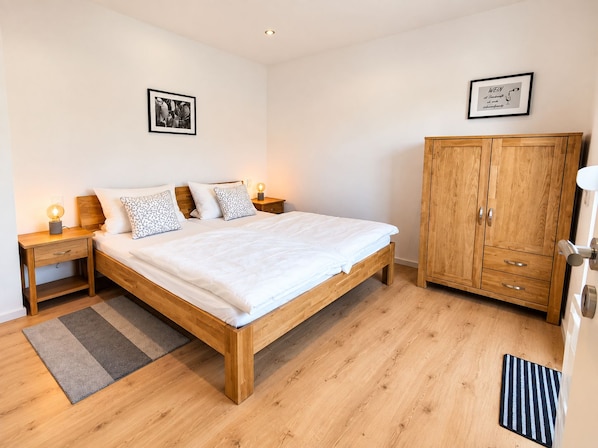 A bedroom with a wooden bed, nightstands, a wardrobe, and two framed pictures on the wall.