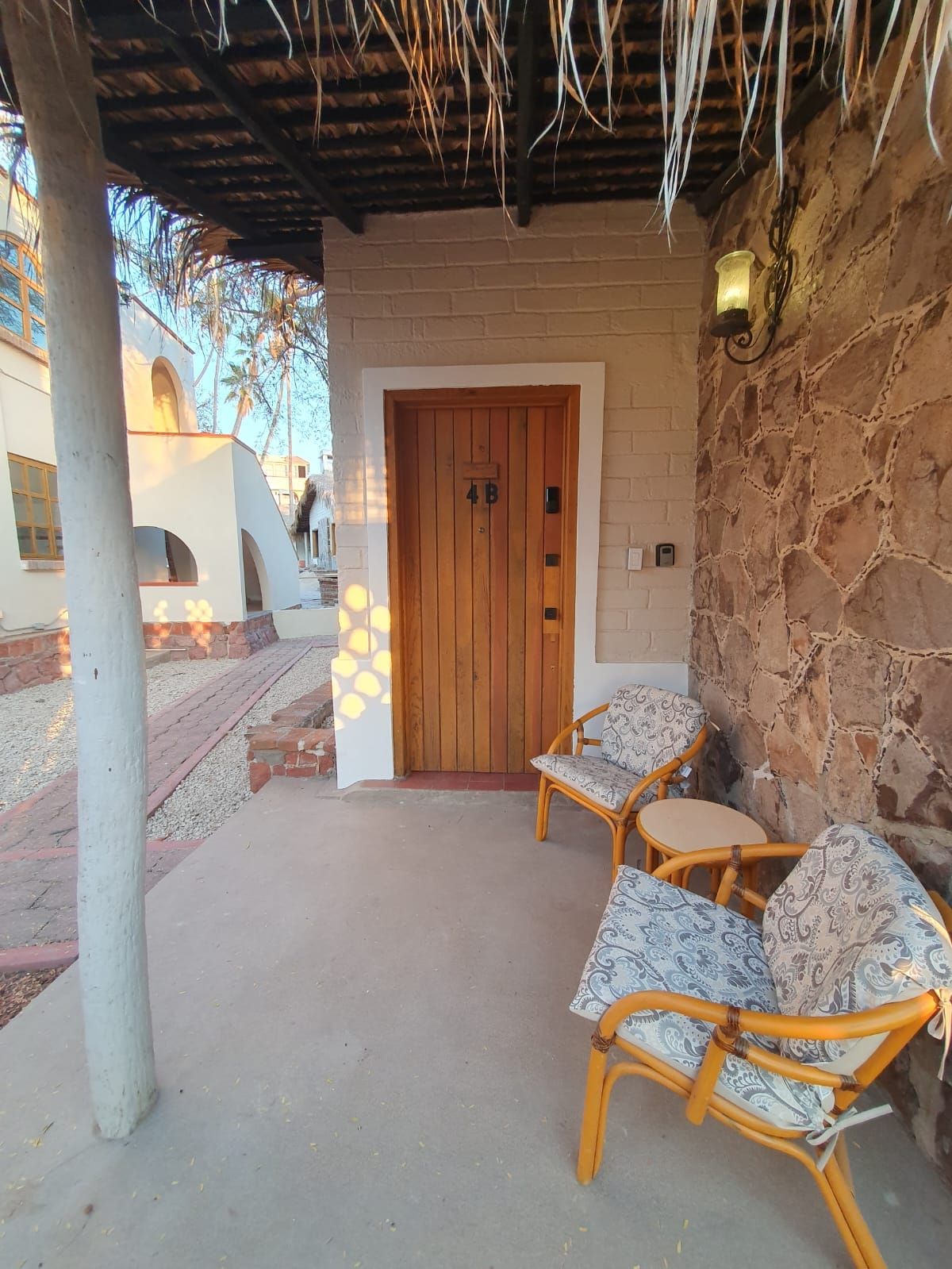 A covered outdoor seating area with a wooden door, stone wall, and a concrete floor.