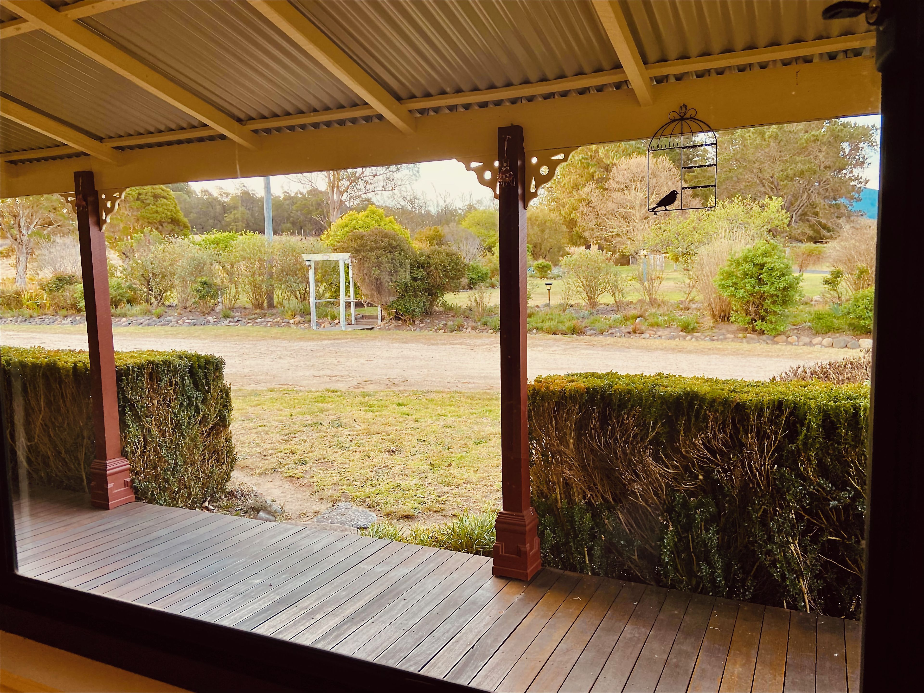 A covered outdoor area with a wooden deck, a pergola structure, and a view of a landscaped garden with various plants and a pathway.