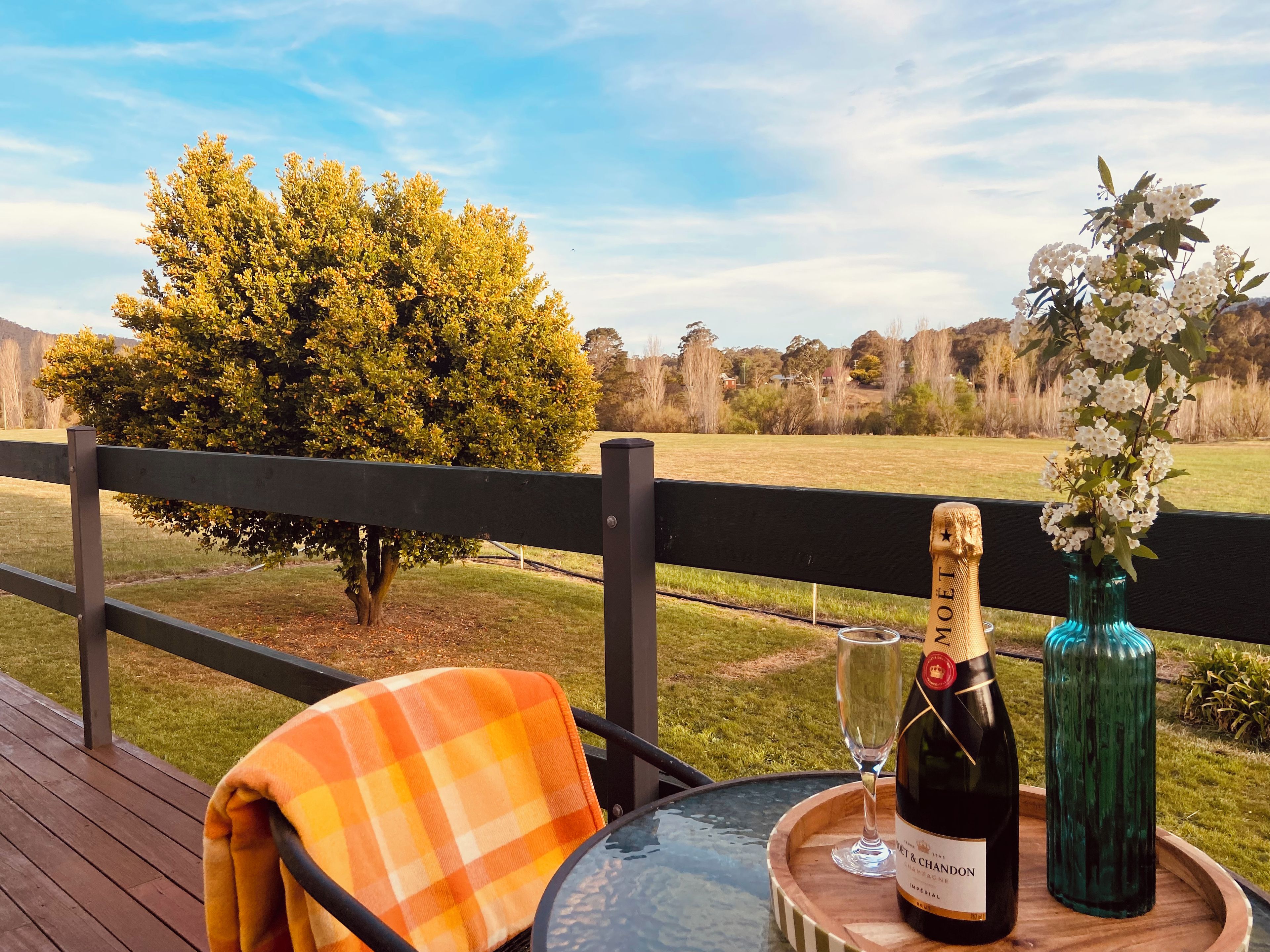 Een tafel met een champagnefles, een glas en een bloemenvaas op een houten dienblad.