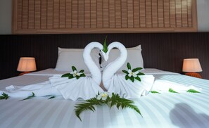 Ein ordentlich bezogenes Bett mit Handtüchern, die zu Schwänen geformt sind, einem Kopfkissen und einer Zierblume.