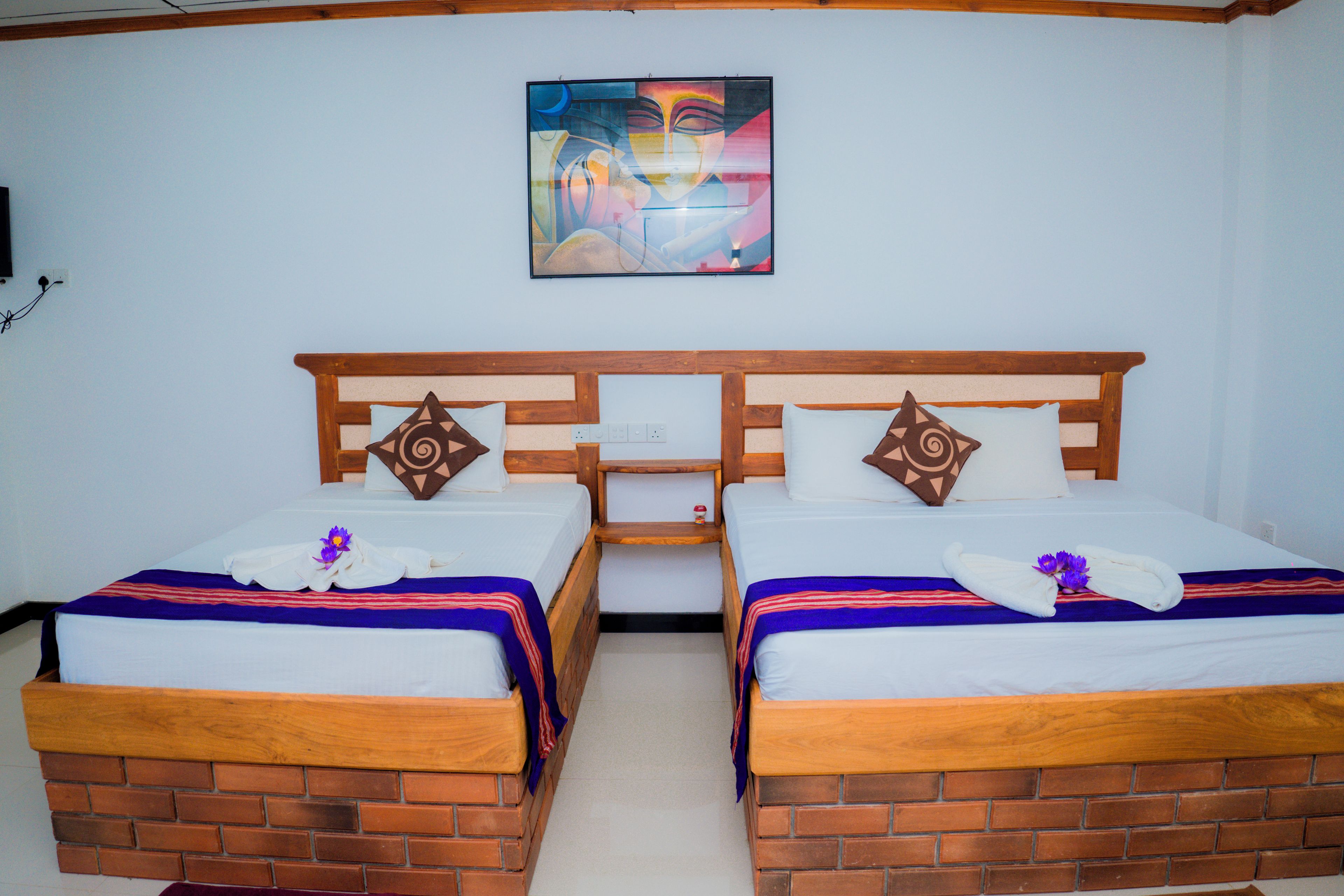 A hotel room with two wooden beds, a brick accent wall, and a painting on the wall.