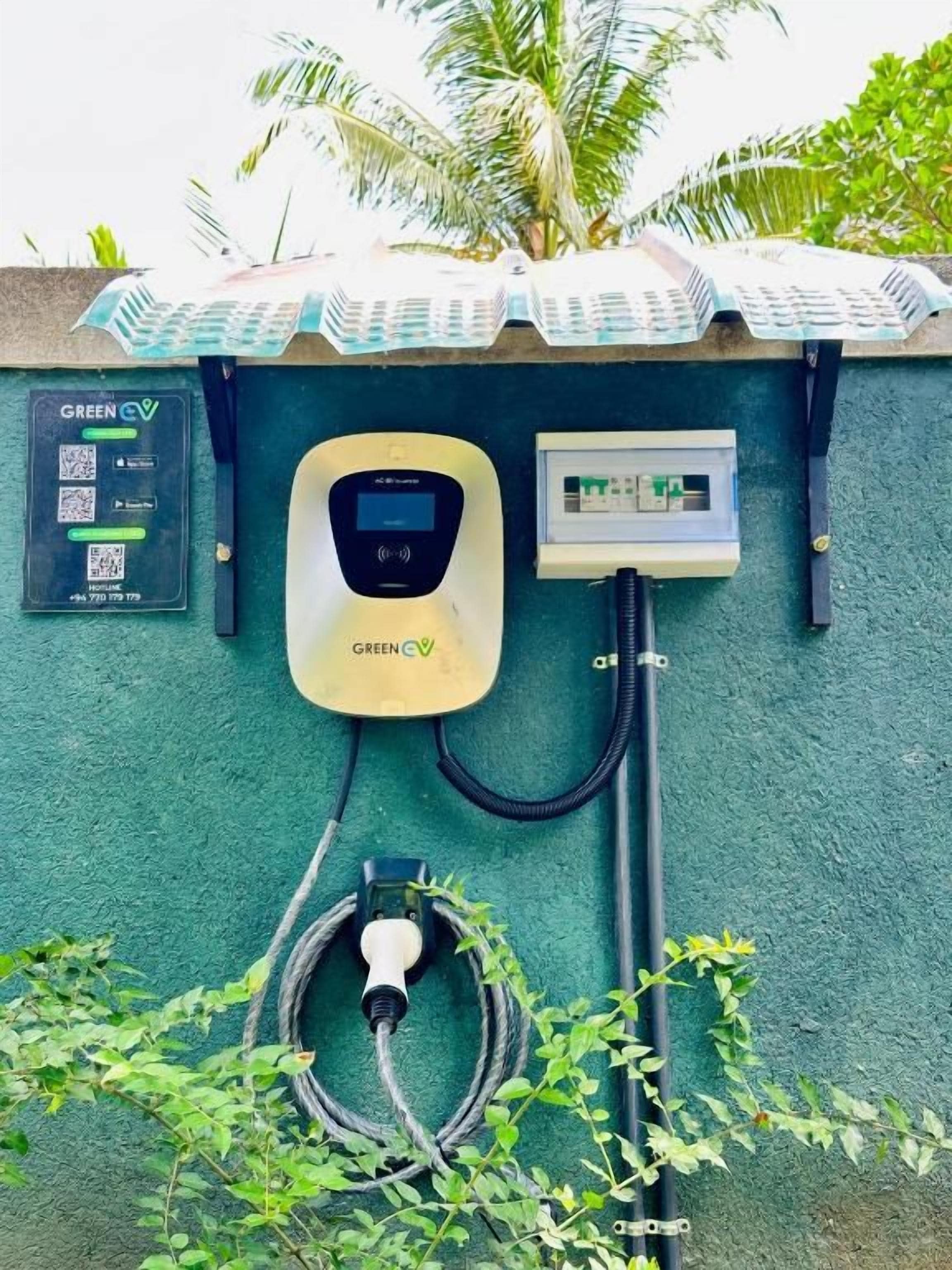 A wall-mounted electric vehicle charging station with a control panel, a QR code, and a cable connected to a power source.